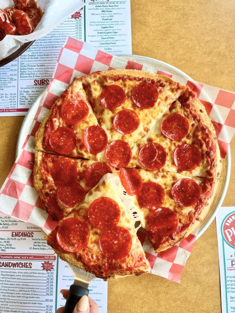 Pepperoni pizza cut into slices on with red and white checkered paper.